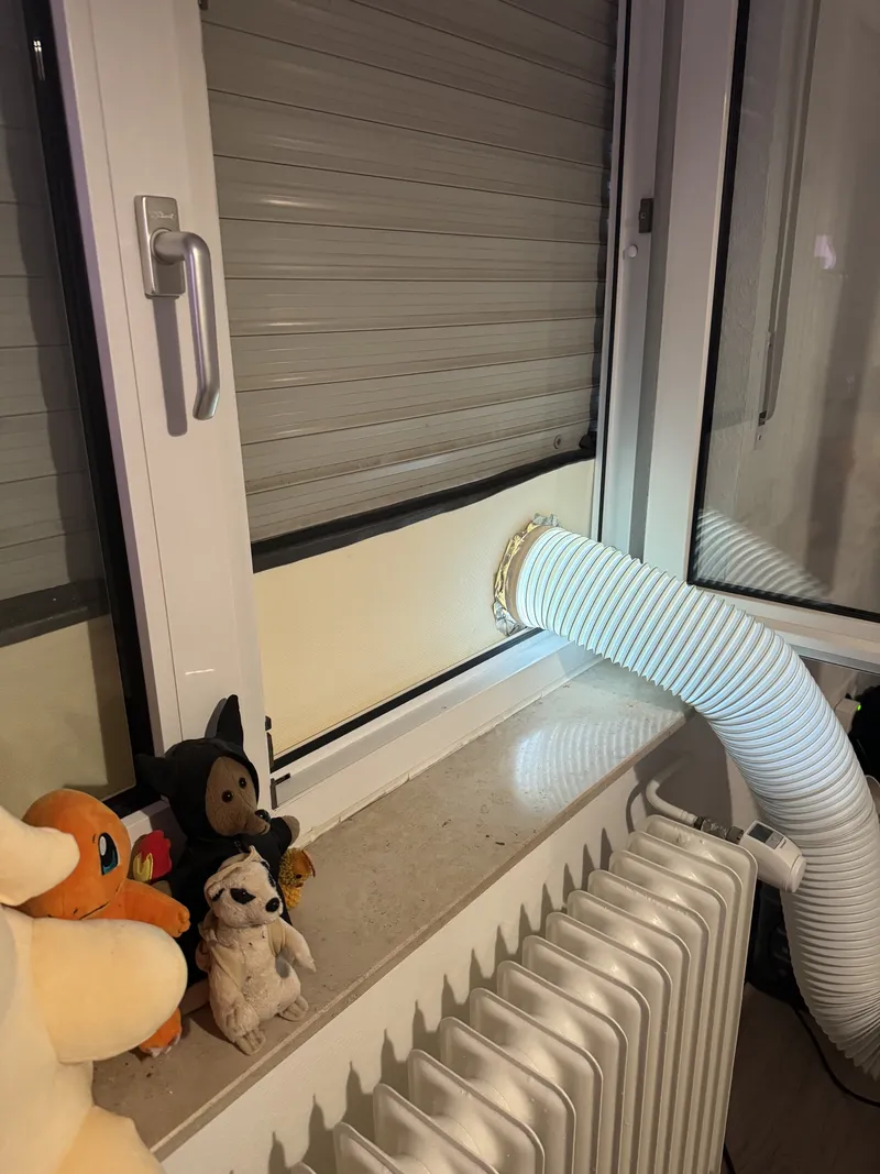 Looking down at the windowsill: roller blind partway down, the XPS panel wedged into the opening with the hose running through it